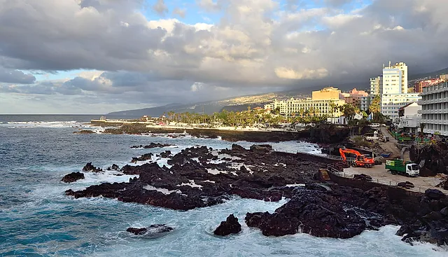 Black volcanic rocks and waves on the coast of Puerto de la Cruz in the afternoon light, with the town behind